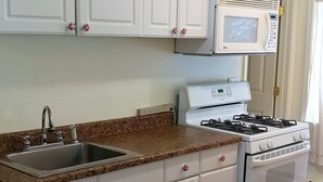 A kitchen with white cabinets, a granite countertop, a stove, and a microwave. - Bird Creek Motel (Indian)