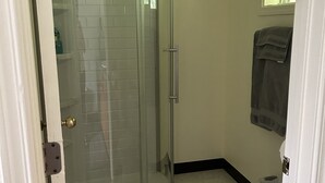 A bathroom with a glass shower enclosure, a toilet, and a towel hanging on the wall. - Bird Creek Motel (Indian)