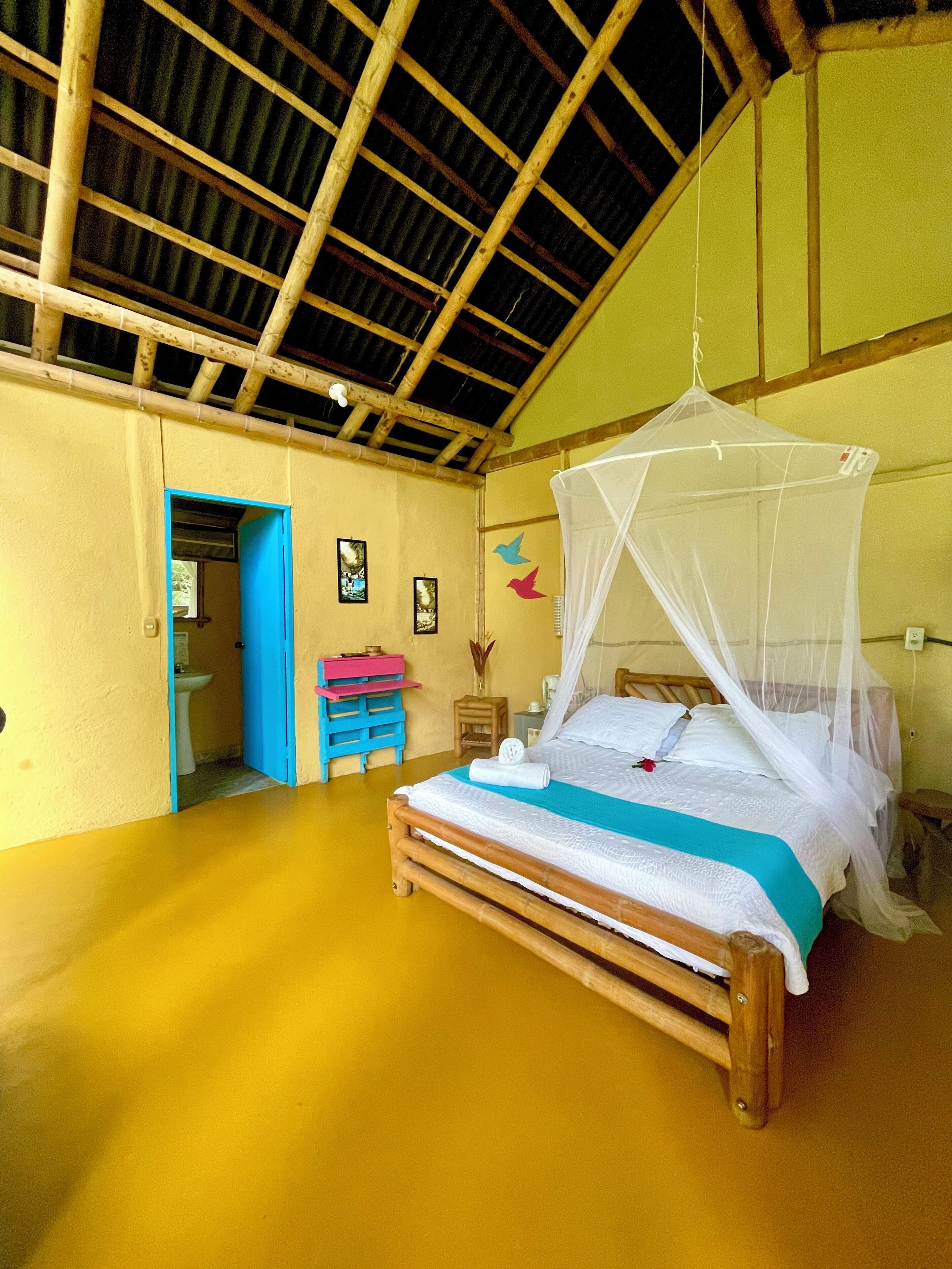 A room with a bed under a mosquito net, a wooden ceiling, and a door leading to another room.