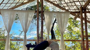 Una terraza de madera con una zona cubierta, mostrando a una persona realizando una postura de yoga.