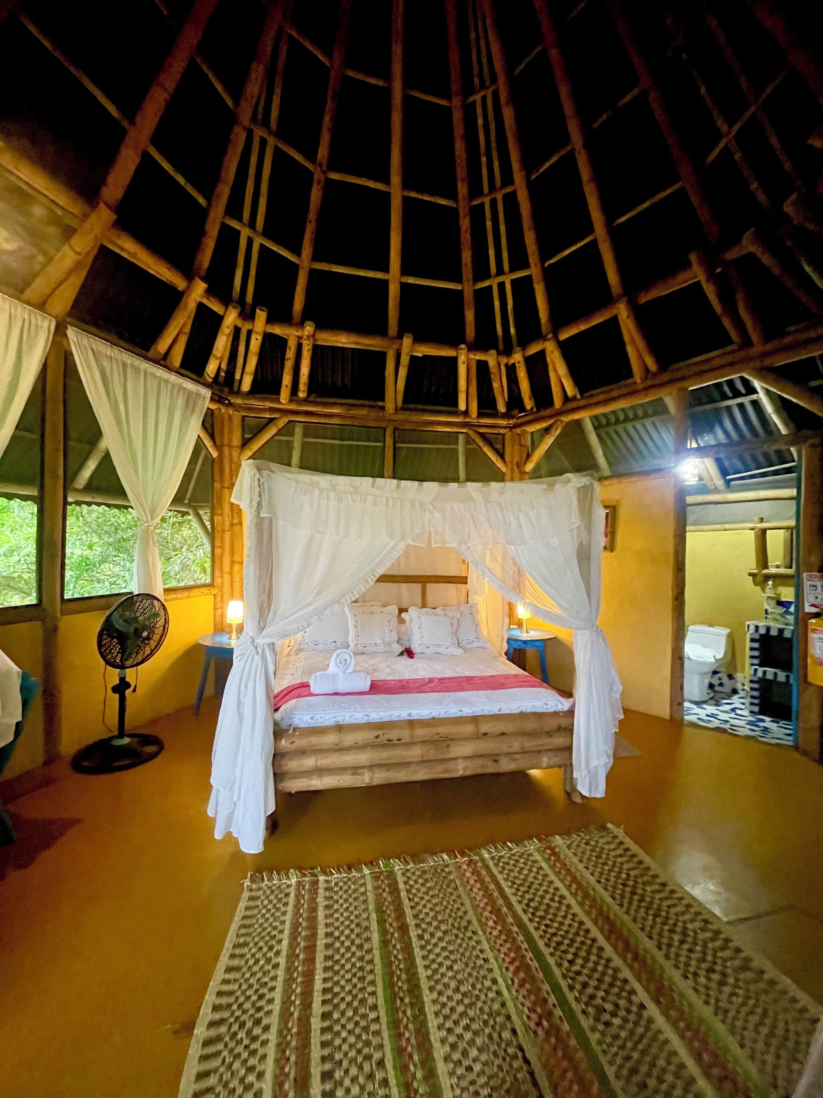 A bed with a canopy, a standing fan, and a bedside table with a lamp.