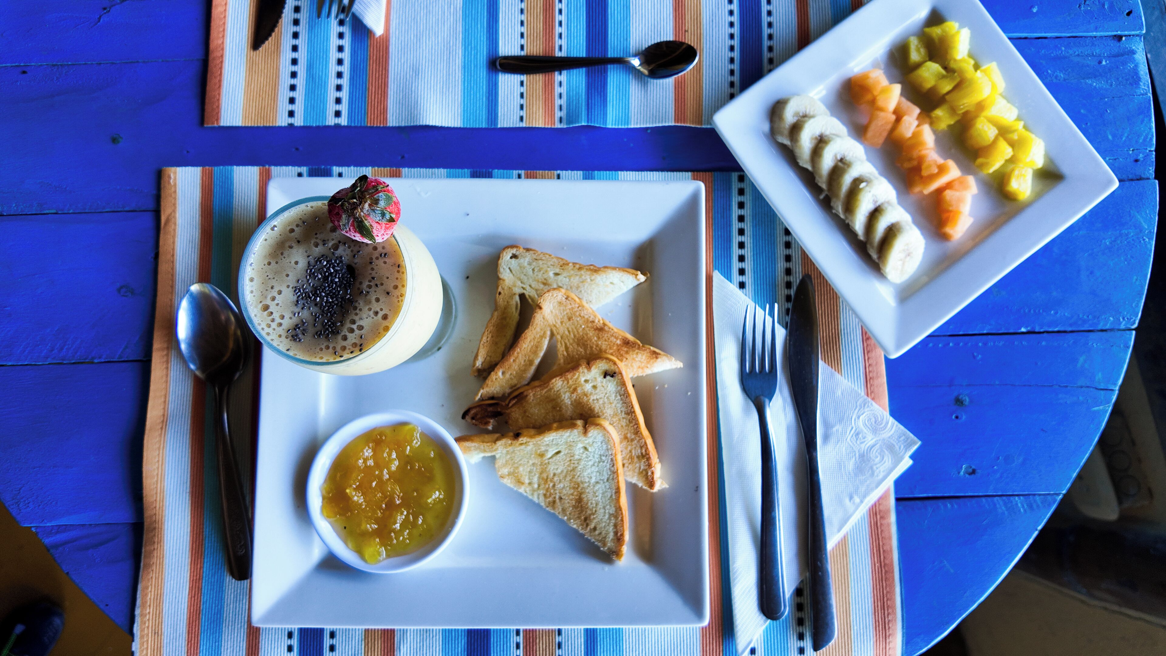 Een ontbijtbord met toast, een fruitschaal en een smoothie.
