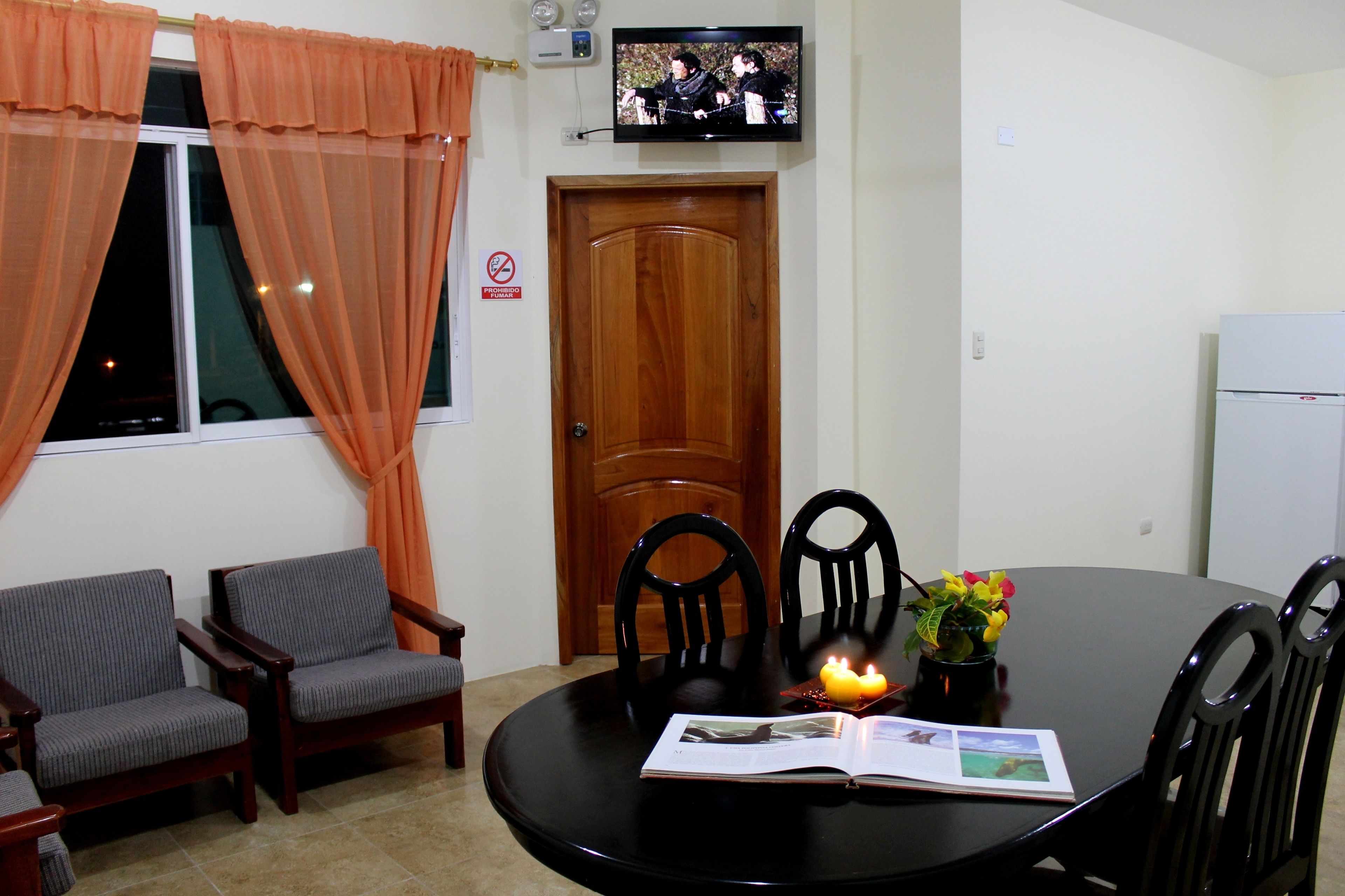 Un comedor con una mesa redonda, dos sillas, un televisor sobre la puerta y una planta pequeña sobre la mesa.