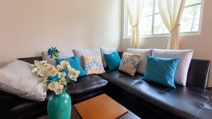 Una sala de estar moderna con un sofá de cuero negro, una mesa de centro de madera y un jarrón con flores blancas.