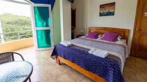 Un dormitorio con cama, televisión, un cuadro y balcón con vistas a la vegetación.