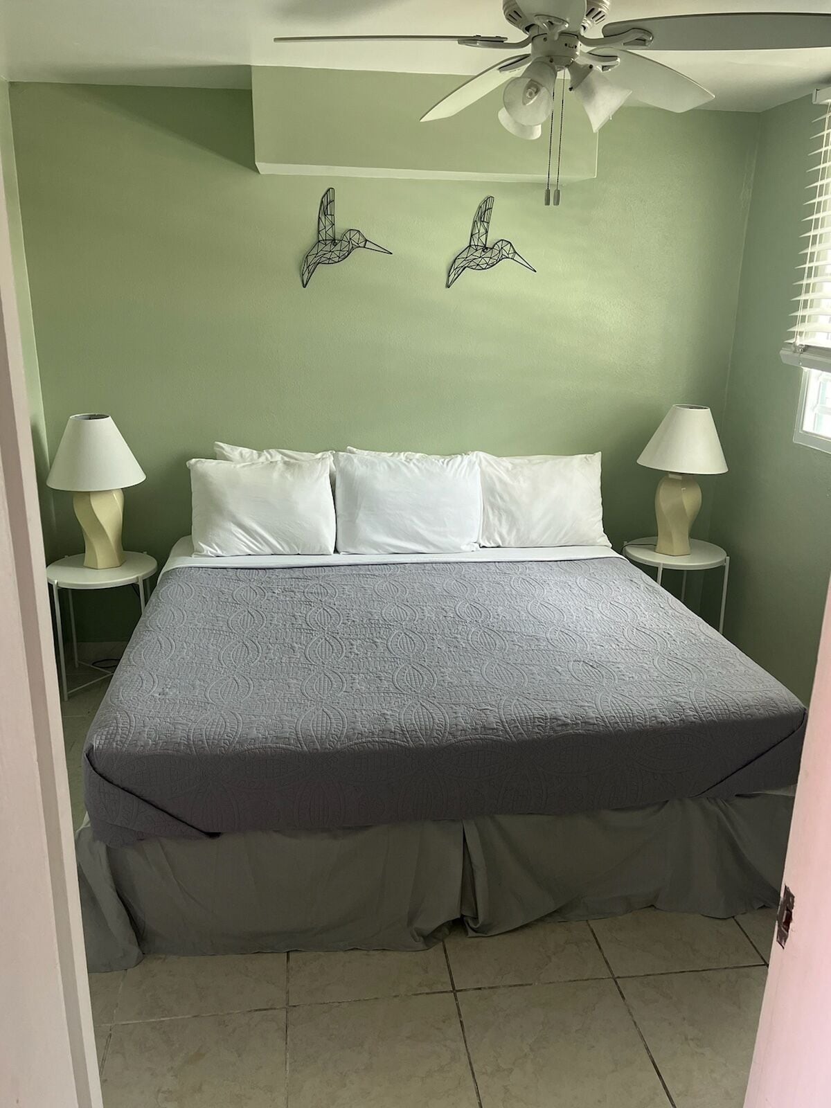 A bedroom with a bed, two wall-mounted bird sculptures, a ceiling fan, and two bedside lamps.