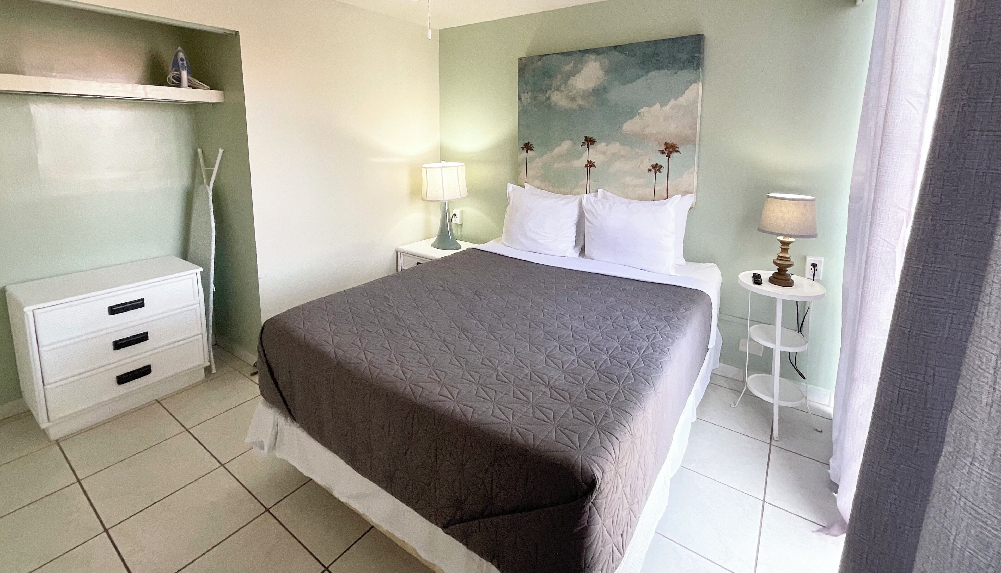 A neatly arranged bedroom with a bed, bedside tables, a lamp, and a painting on the wall.