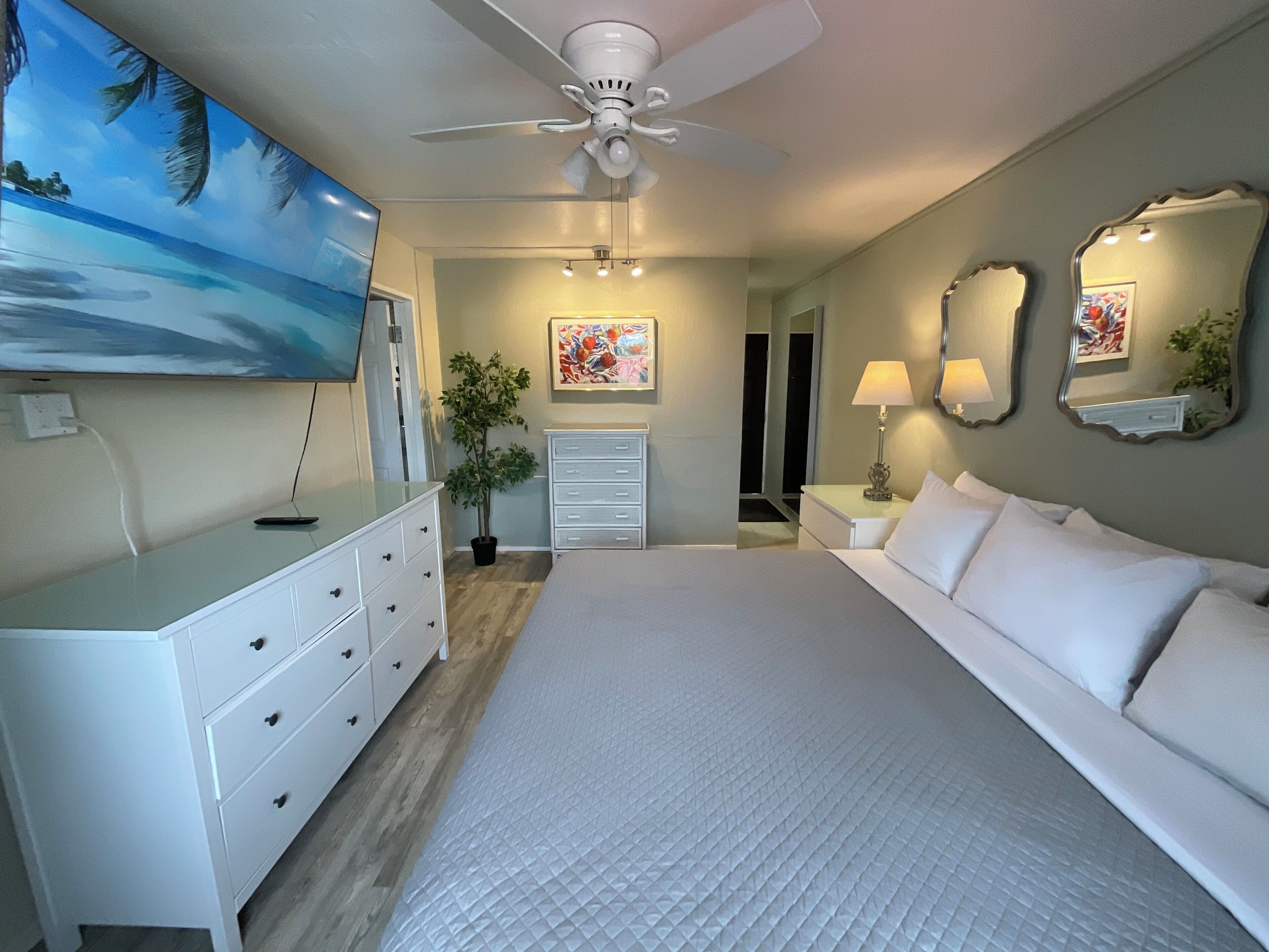 A bedroom with a bed, dresser, ceiling fan, and artwork.