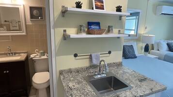 A modern bathroom with a sink, toilet, and a vanity. There are shelves above the sink with decorative items.