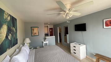 A hotel room with a bed, a ceiling fan, a TV, and a desk.