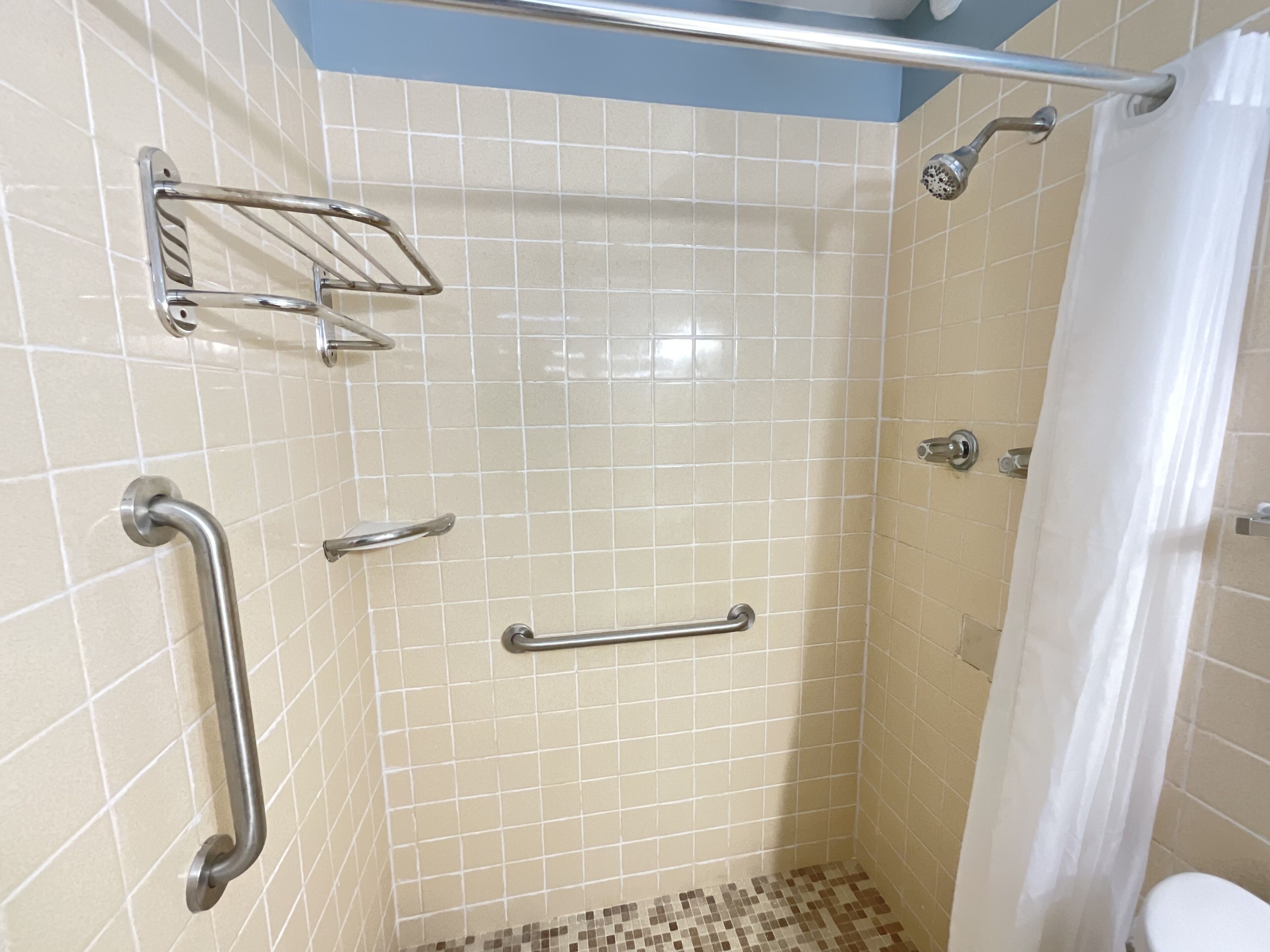 A shower with grab bars, a showerhead, and a tiled floor.