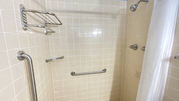 A shower with grab bars, a showerhead, and a tiled floor.