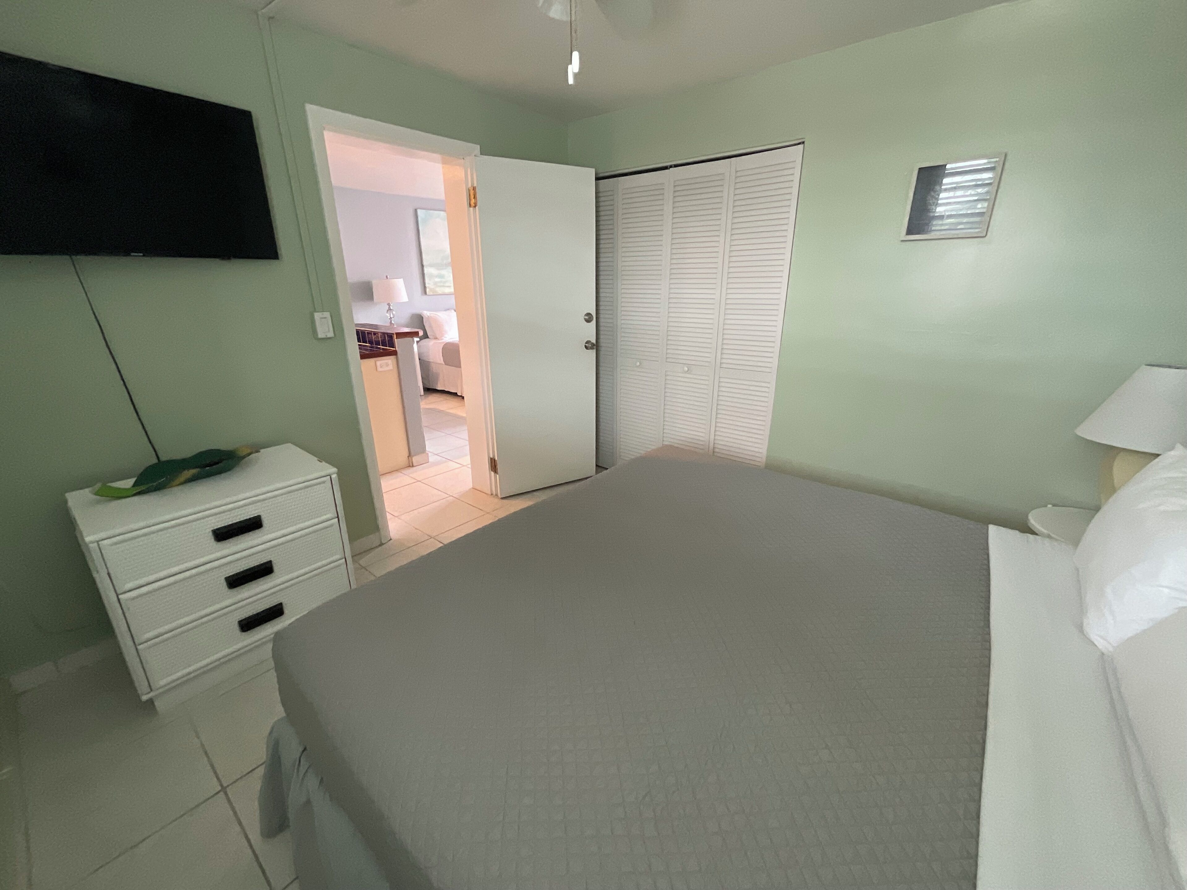 Une chambre à coucher comprenant un lit, une commode, un téléviseur fixé au mur et un placard.