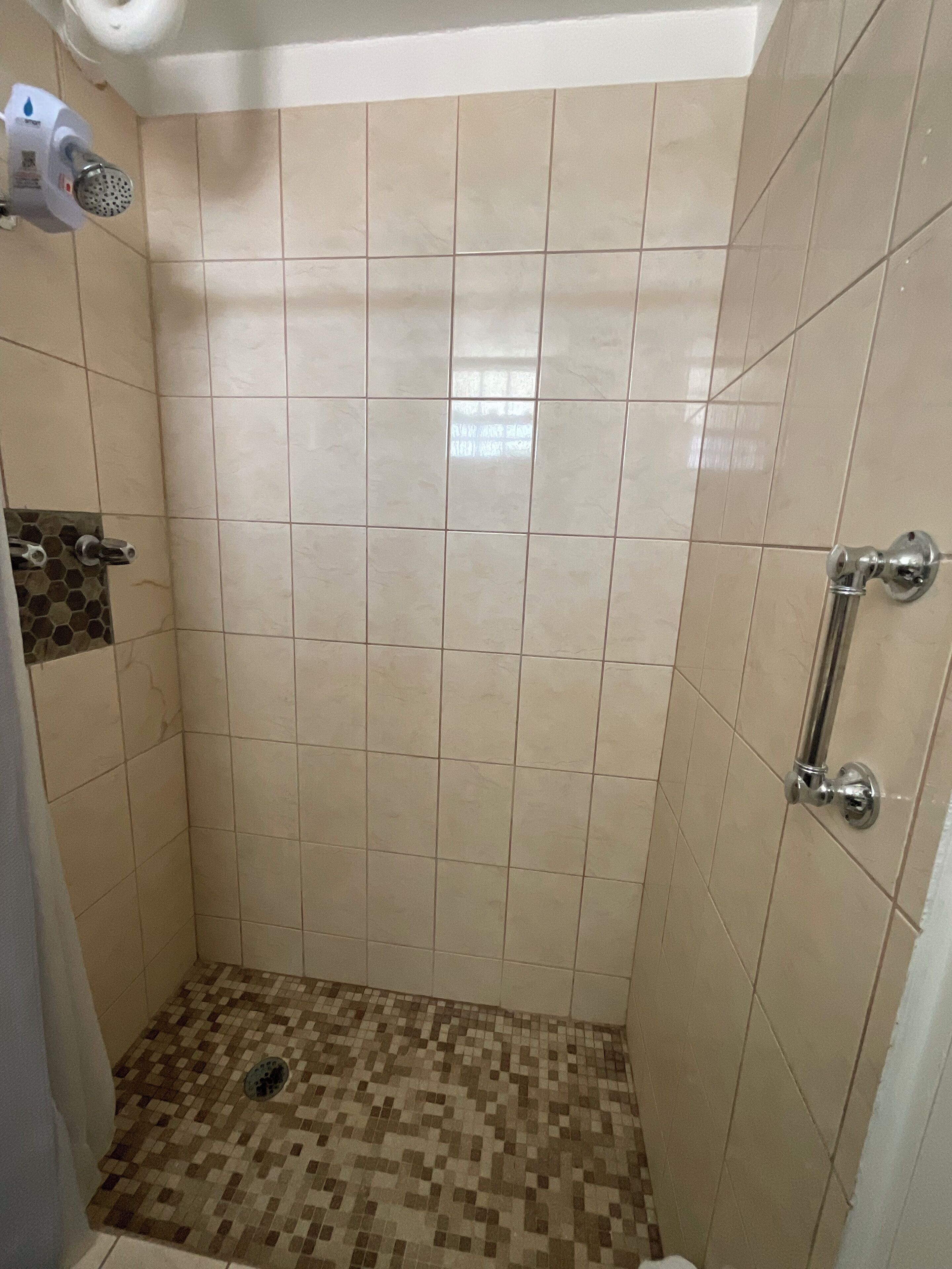 A small, tiled shower area with a handrail and a showerhead.