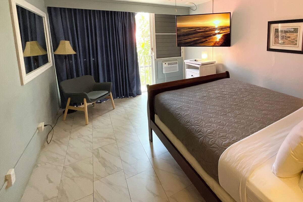 Habitación de hotel con cama, escritorio, silla, televisión y ventana con cortinas.