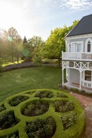 Una casa con fachada blanca, un balcón y un jardín bien cuidado con un laberinto de setos.