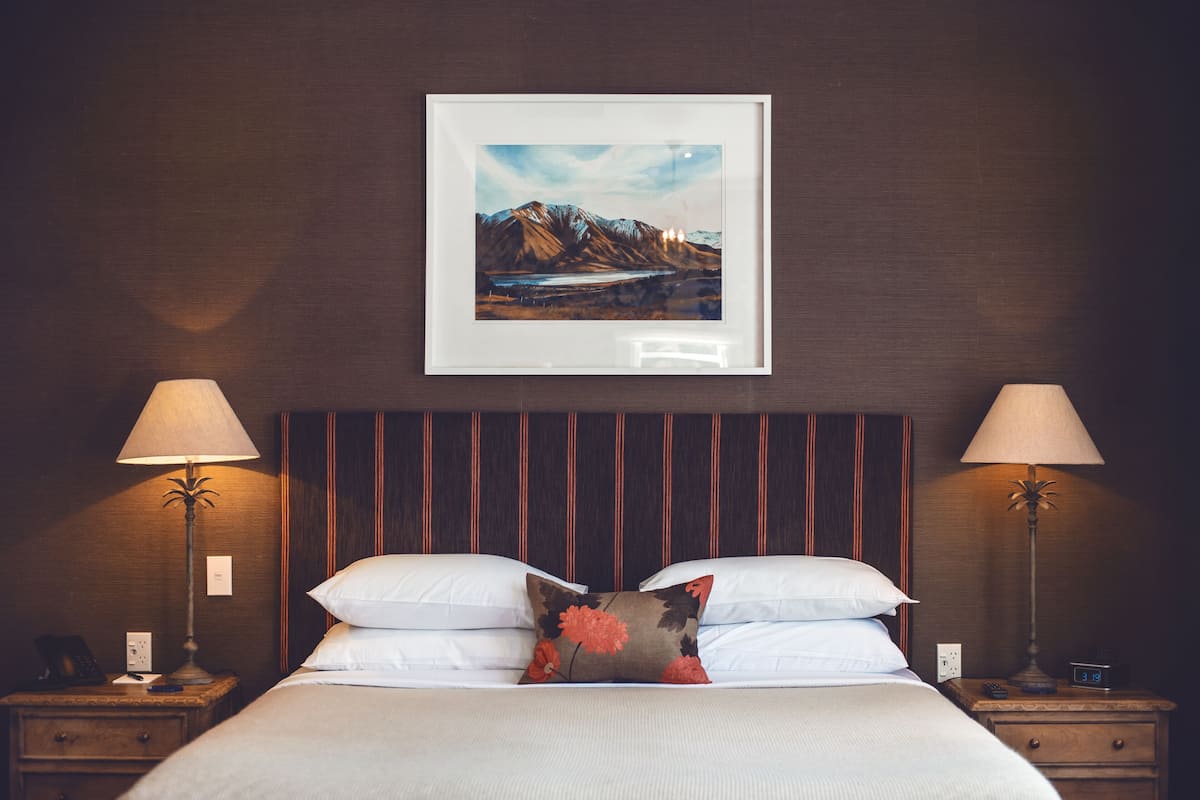 A neatly made bed with white linens and a floral pillow, flanked by two bedside tables with lamps, one of which has a digital clock.