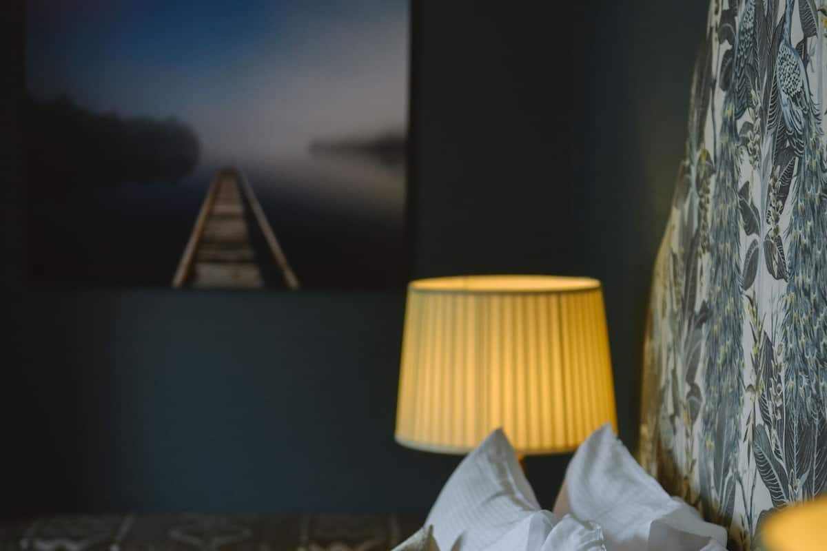 A bedroom with a bed, pillows, a lamp, and a painting on the wall.