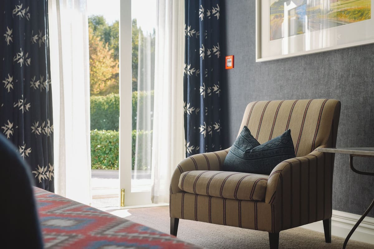 A room with a striped armchair, a patterned rug, and a large window with curtains.