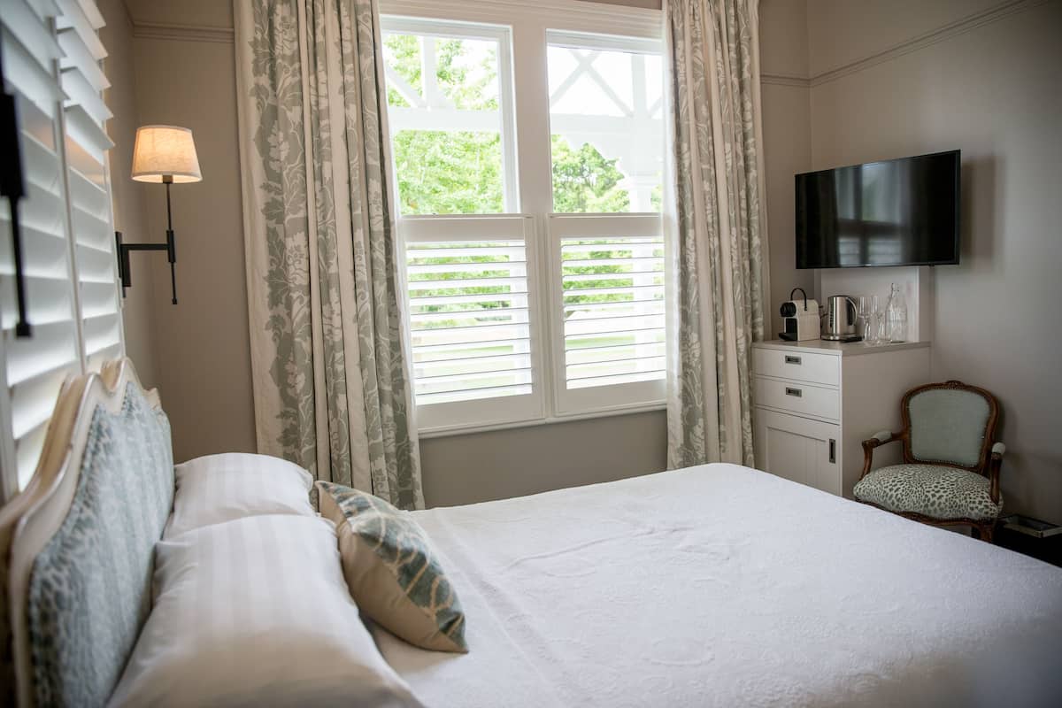 A bedroom with a bed, a nightstand, a chair, a TV, and a window with curtains.