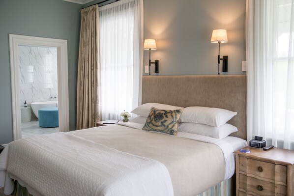 Habitación de hotel con una cama grande, dos lámparas de noche, una mesita de noche y vistas al baño.
