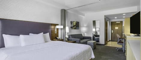 A hotel room with a large bed, a desk, a chair, a sofa, and a television.