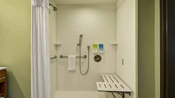 Il y a un espace douche équipé d’un pommeau de douche blanc, d’un pommeau de douche à main et d’un flexible de douche à main. Un porte-serviettes est fixé au mur, et une serviette blanche y est suspendue.