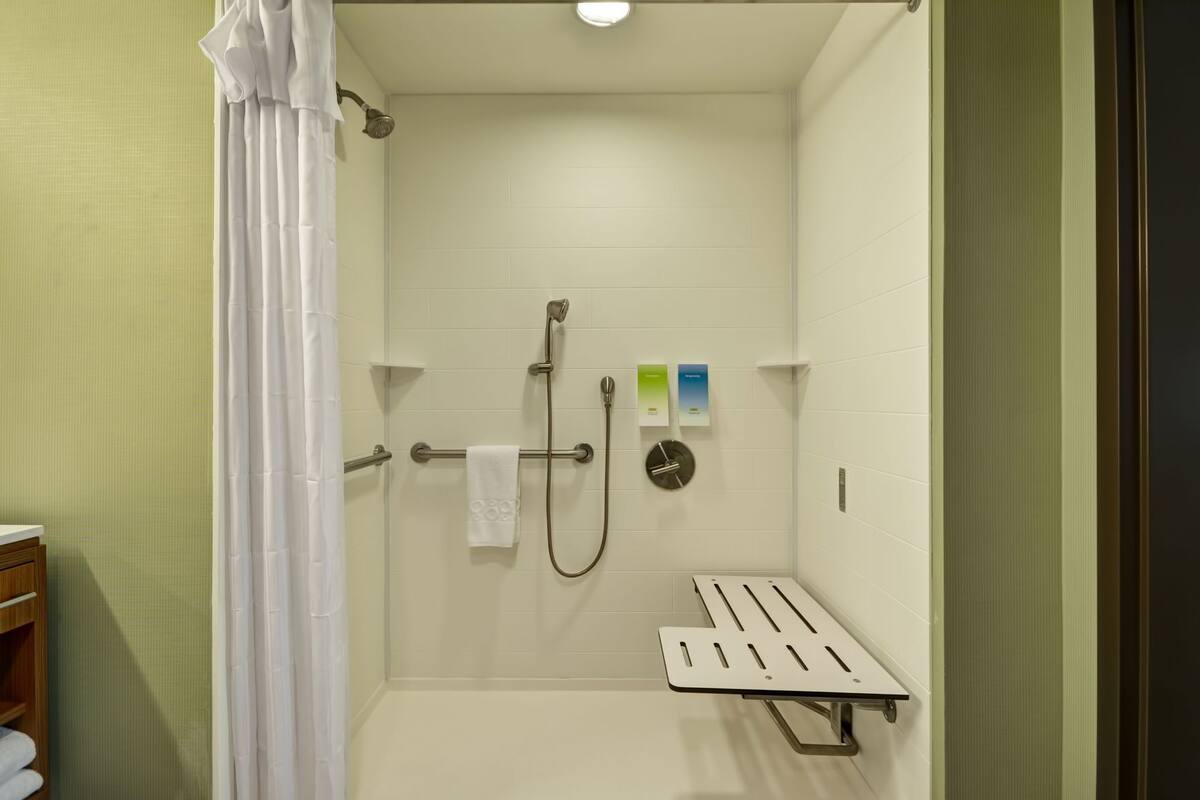 A shower area with a handheld showerhead, a towel rack, and a shelf.