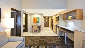 Una habitación de hotel compacta con kitchenette, zona de comedor y sala de estar con sofá y lámpara.