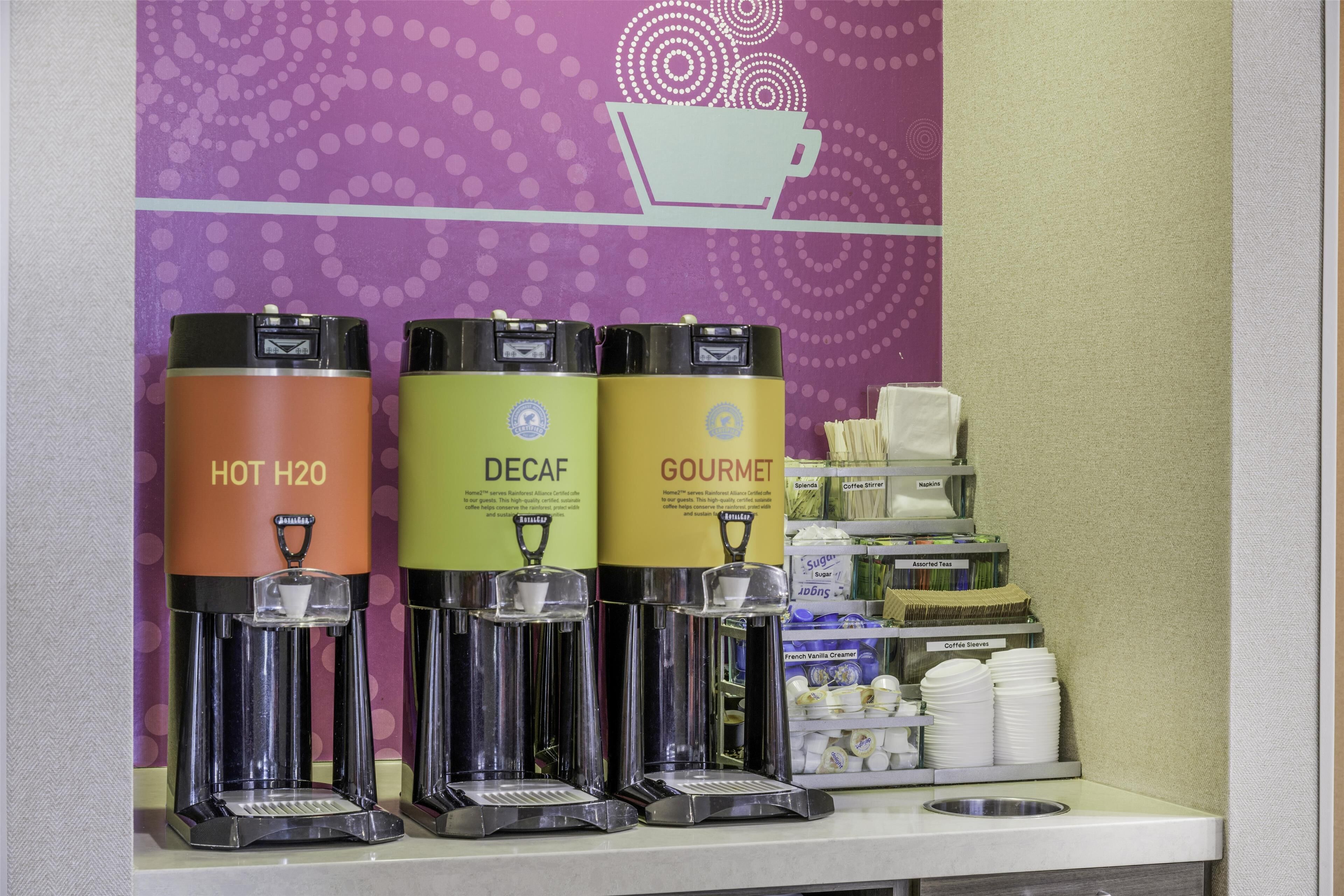 Three beverage dispensers labeled "HOT H2O," "DECAF," and "GOURMET" in a commercial setting.