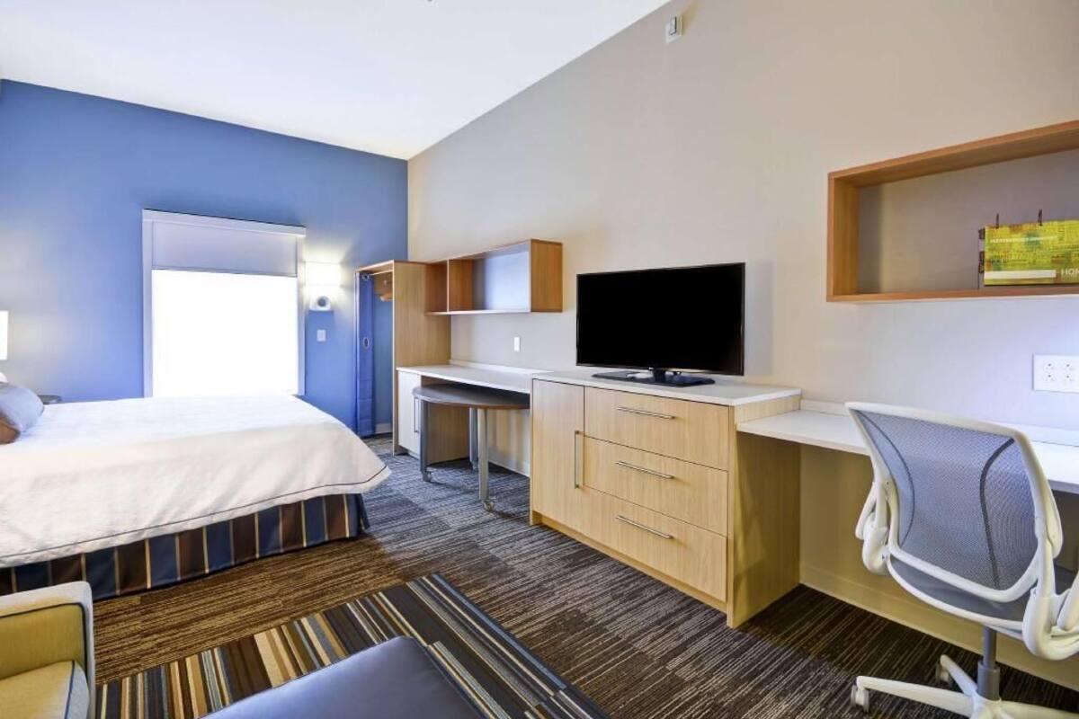 A hotel room with a bed, desk, chair, television, and a bookshelf.