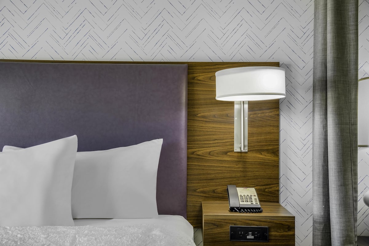 A hotel room with a bed, a nightstand with a lamp, and a phone.