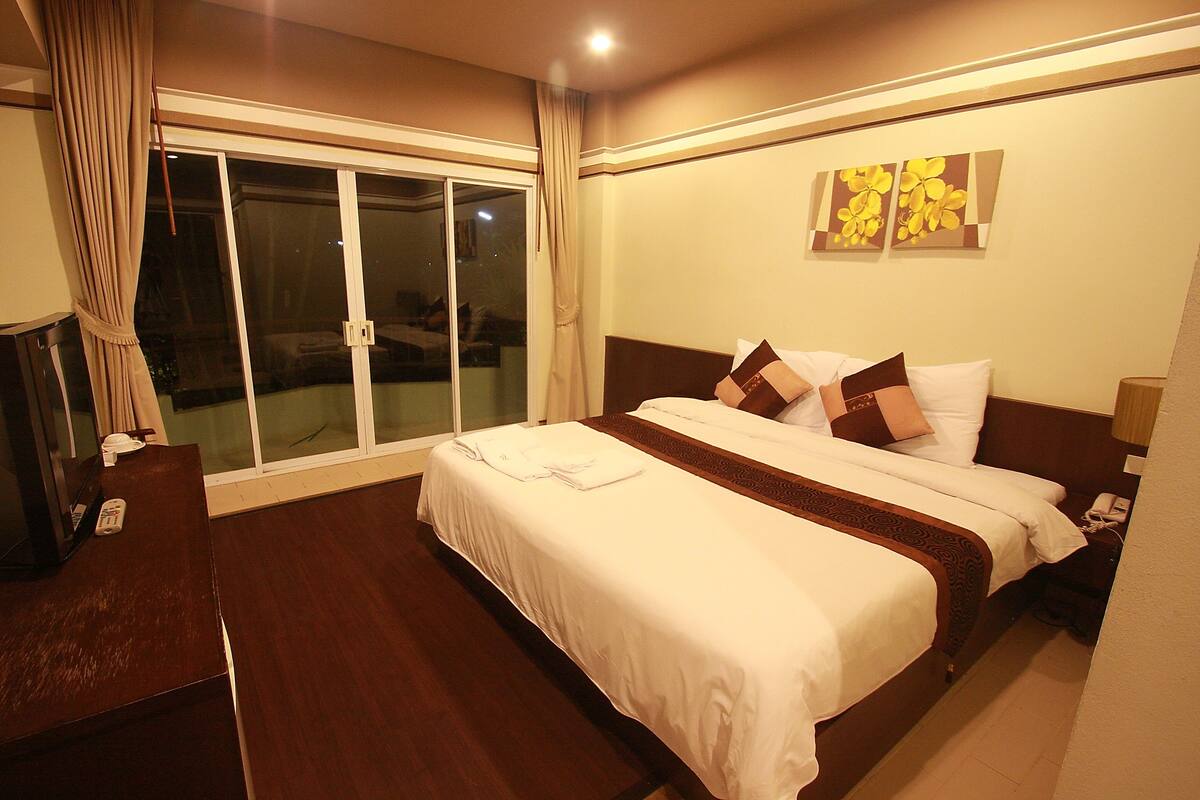 A hotel room with a large bed, a desk, and a view of a balcony.