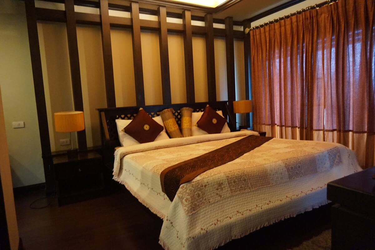 A neatly made bed with a white and brown blanket, two pillows, and a wooden headboard. There are two bedside lamps and a nightstand with a lamp.