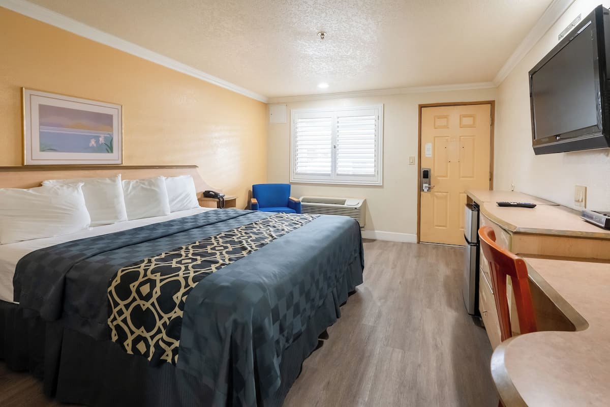 A hotel room with a bed, a desk, a chair, a TV, and a window with blinds.