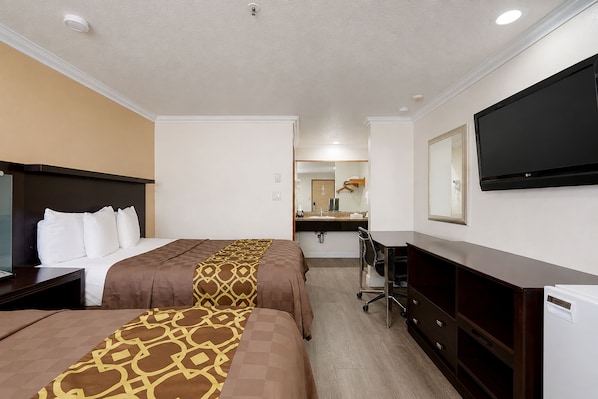 Quarto de hotel com duas camas, uma escrivaninha, um penteoudeiro, um espelho e uma televisão.