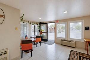 Un hall d’hôtel avec un comptoir d’accueil, un espace repas avec des chaises, de grandes fenêtres et un panneau indiquant la sortie.