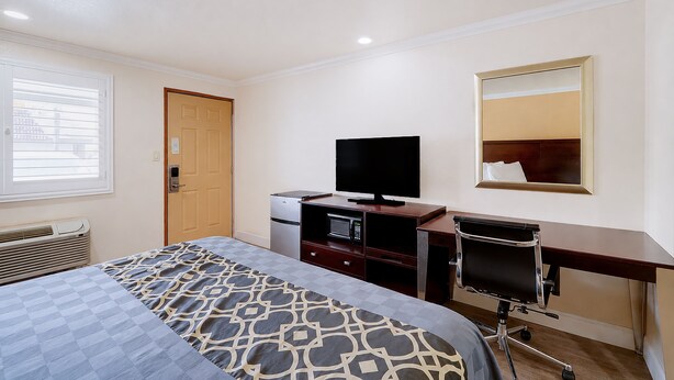 Une chambre d’hôtel équipée d’un lit, d’un bureau, d’une télévision, d’un miroir et d’une fenêtre avec des stores.