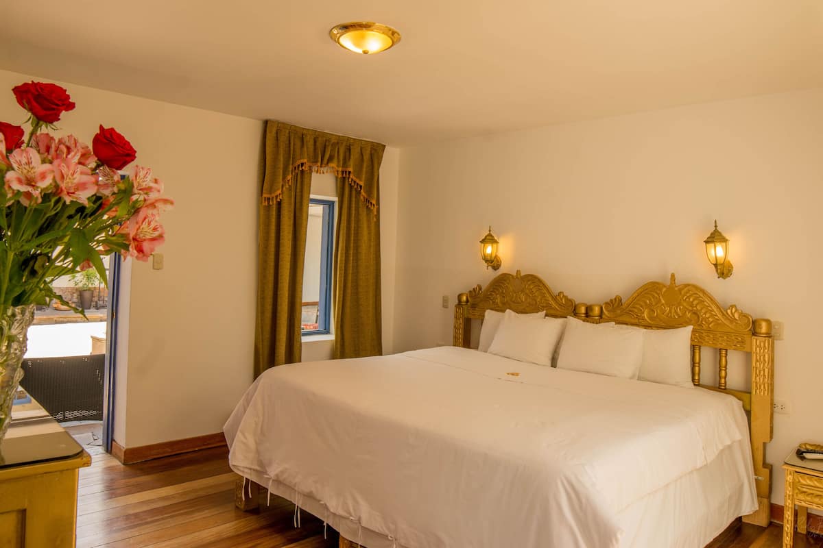A hotel room with a large bed, a vase of flowers, and a window with curtains.
