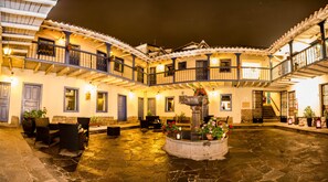 Un patio con una fuente, asientos al aire libre y un edificio con balcones y puertas.