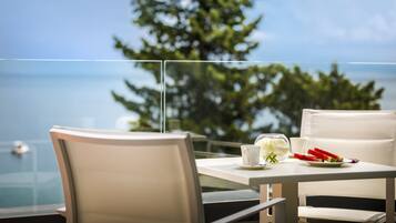 Una mesa de comedor con sillas blancas, un separador de vidrio y vistas al océano y árboles.