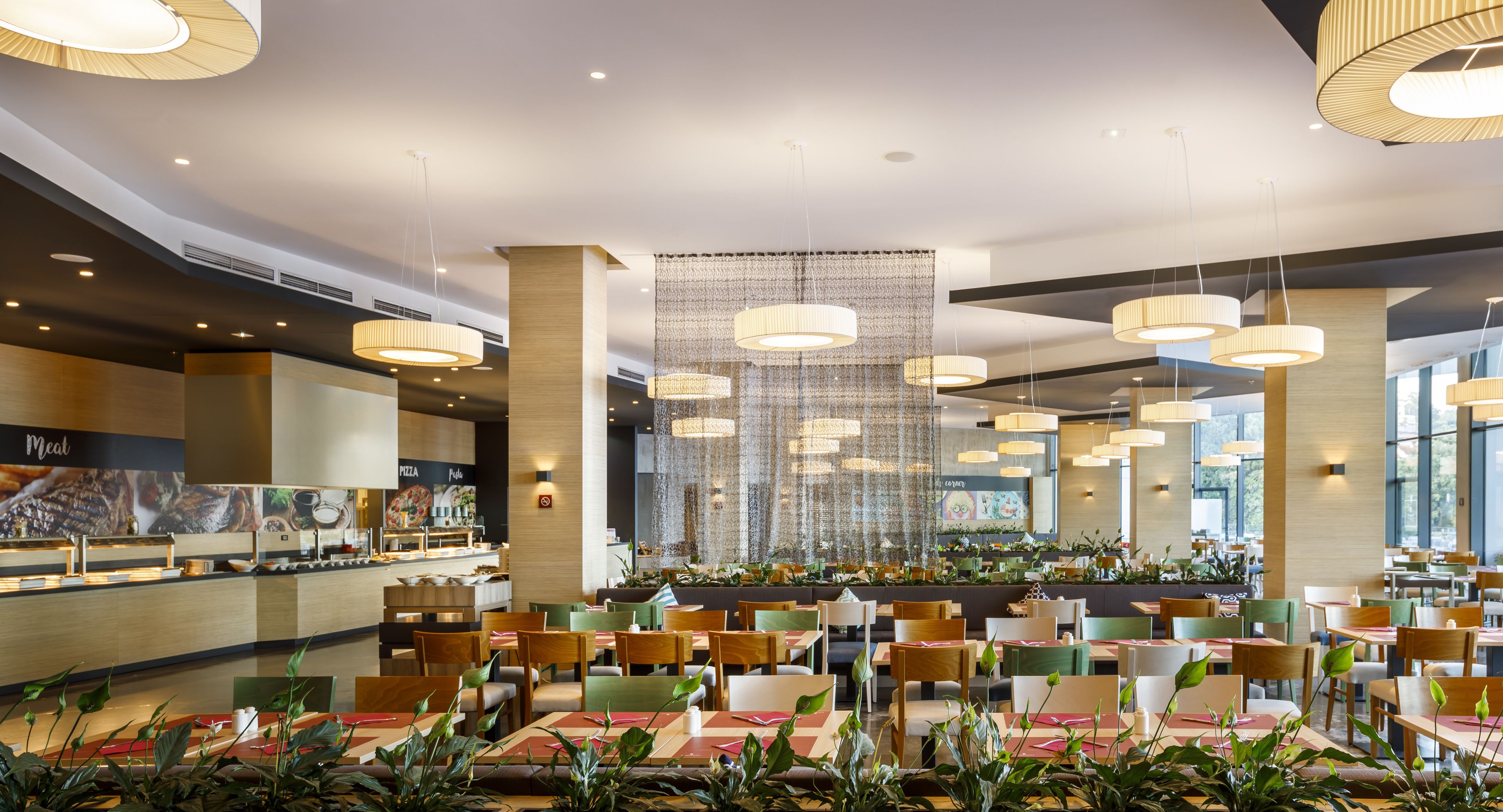 Un restaurante espacioso con varias zonas de comedor, iluminación colgante y una barra de buffet.