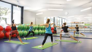 A group of people doing yoga in a well-lit room with large windows and exercise balls.