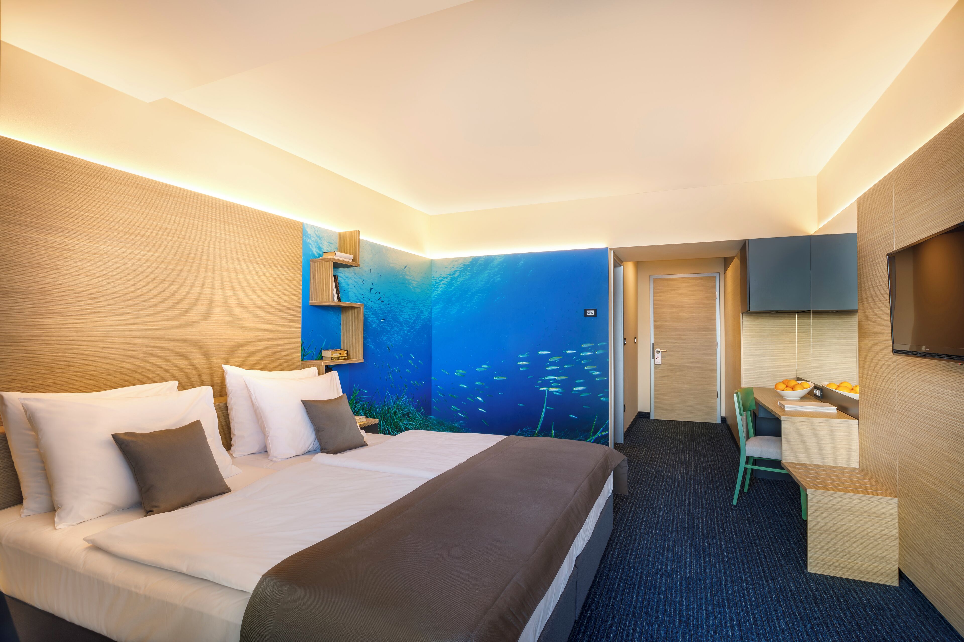 Een moderne hotelkamer met een groot bed, een bureau en een wanddecoratie van een onderwaterscène.