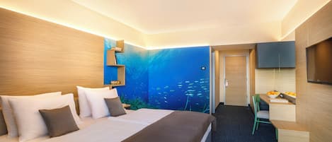Quarto de hotel moderno com uma cama grande, uma escrivaninha e um mural na parede retratando uma cena subaquática.