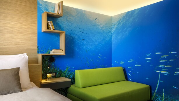 A room with a bed, a green sofa, a nightstand with a lamp, and a wall mural of an underwater scene. - Hotel I čići - Liburnia (Opatija)
