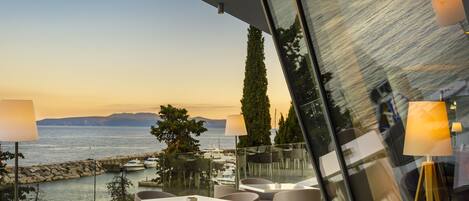 Una terraza con mesas y sillas, con vista a un cuerpo de agua y montañas lejanas.