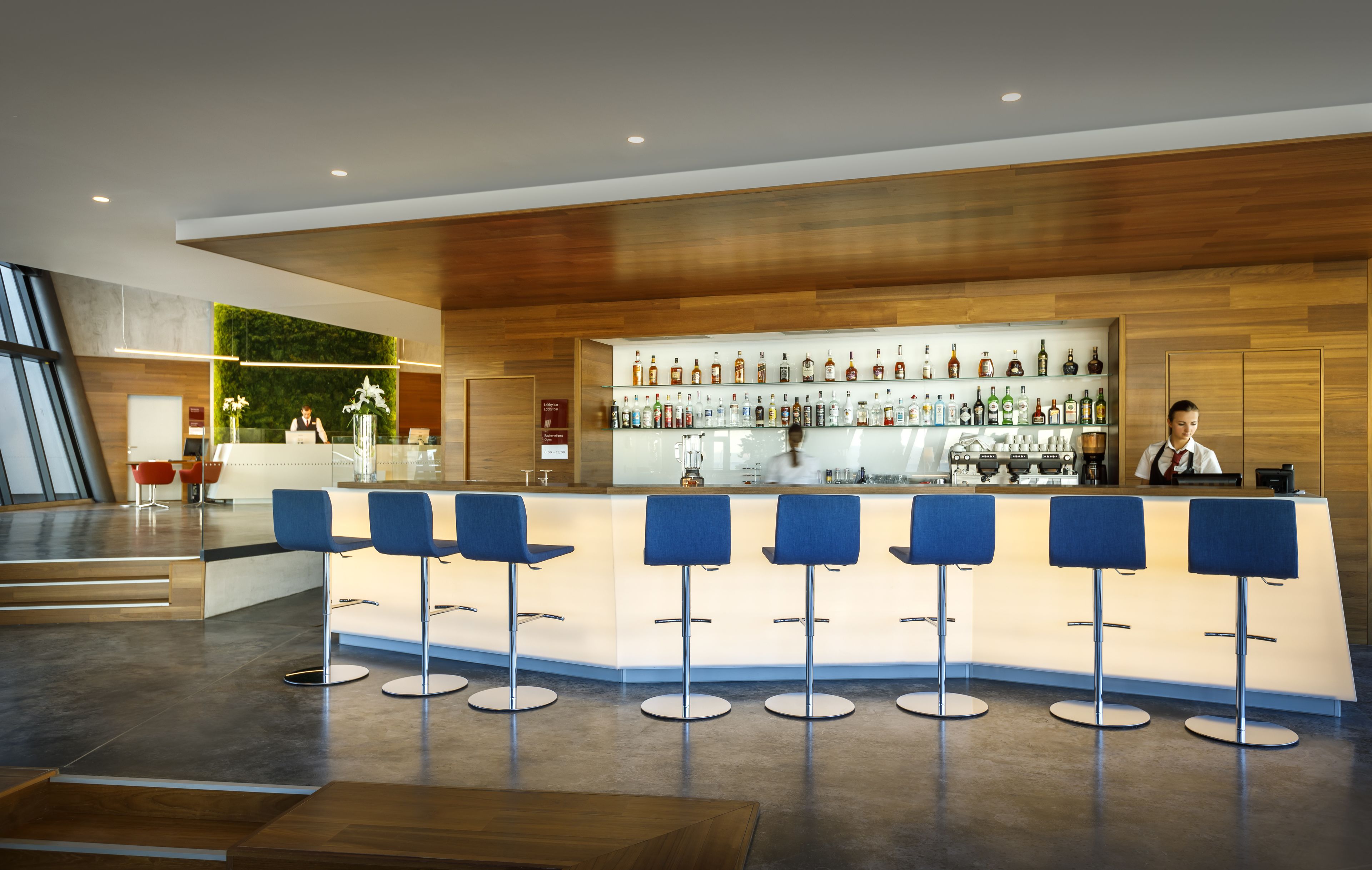 A modern bar area with a wooden ceiling, a glass display case of liquor bottles, and blue bar stools.