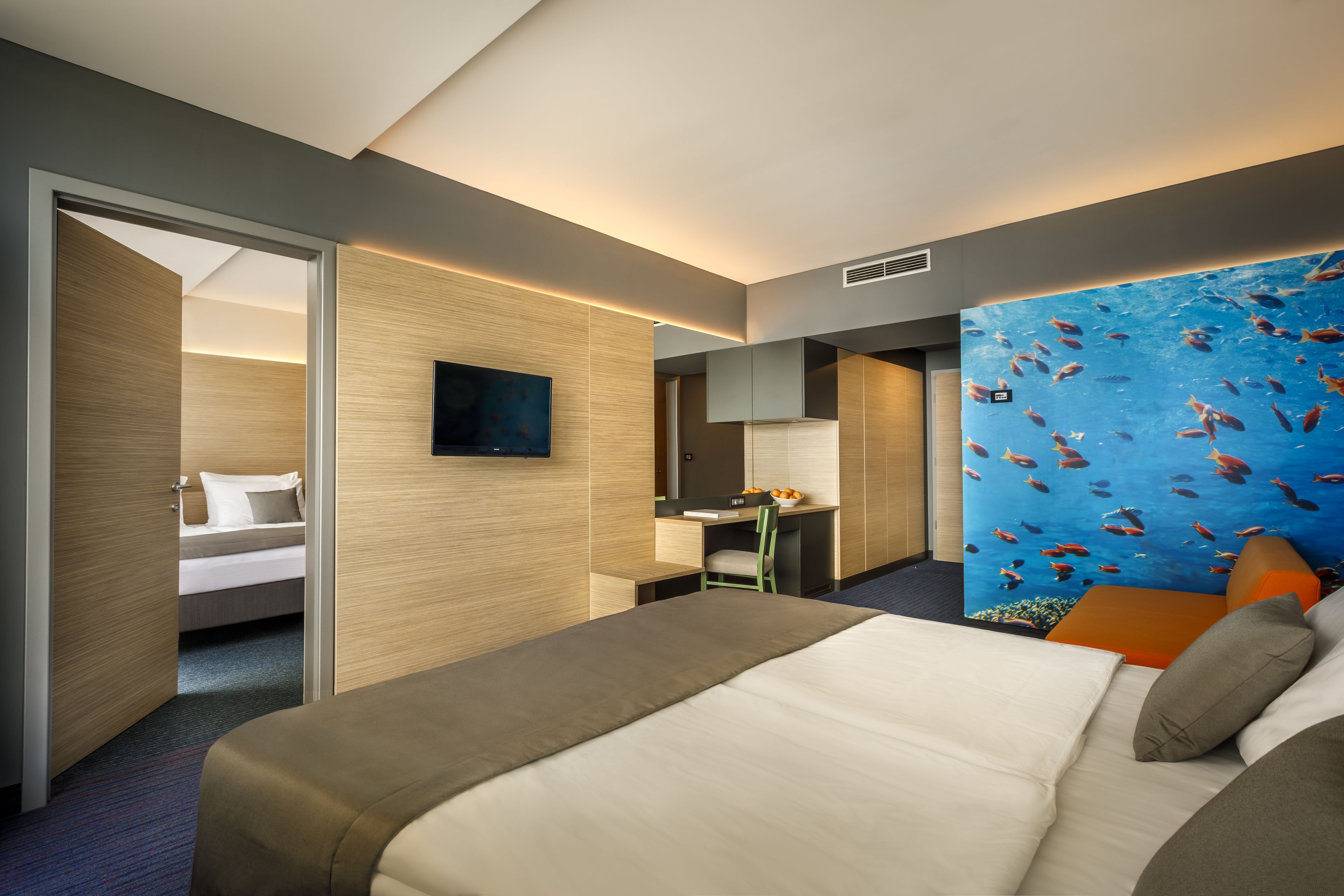 Ein Hotelzimmer mit einem Bett, einem Schreibtisch, einem Sessel, einem Fernseher und einem Wandbild mit Fischen.