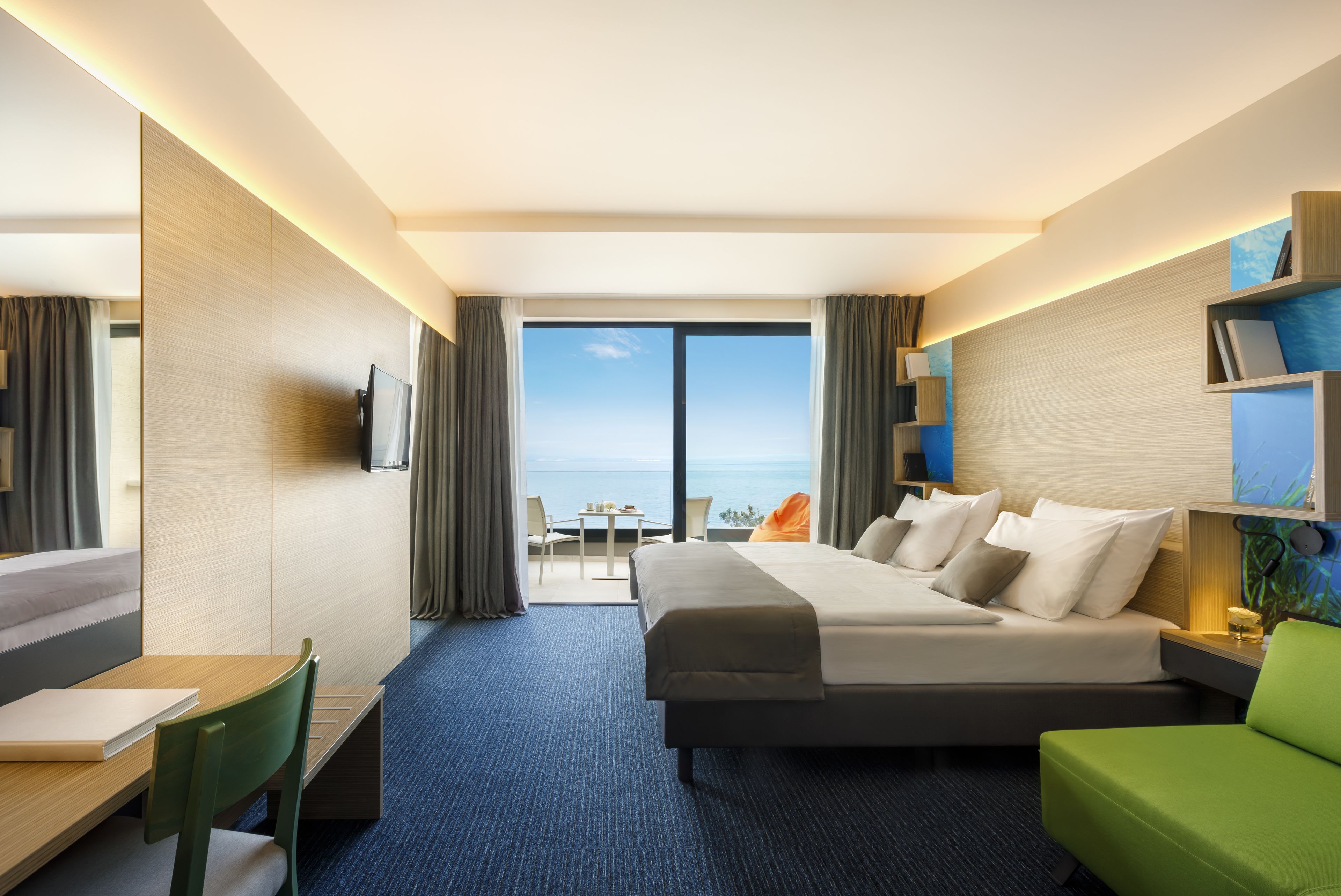 A modern hotel room with a large bed, a desk, and a view of the ocean.